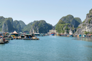 Floating village in Ha Long Bay with limestone karsts in the background and various boats and floating houses on the water