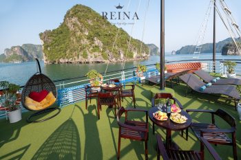 Scenic outdoor deck on the Reina Halong Bay day cruise with lounge chairs, tables with food and drinks, and stunning views of limestone islands