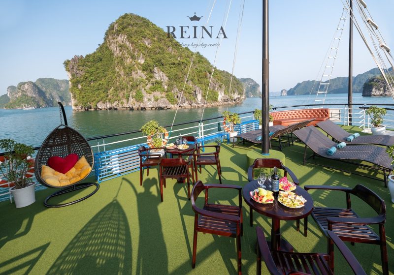 Scenic outdoor deck on the Reina Halong Bay day cruise with lounge chairs, tables with food and drinks, and stunning views of limestone islands