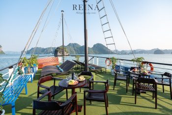 Outdoor deck of the Reina Halong Bay day cruise with lounge chairs, tables with food and drinks, and panoramic views of limestone islands