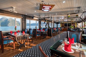 Elegant dining area on the Reina Halong Bay day cruise with set tables, panoramic windows, and scenic views of limestone islands