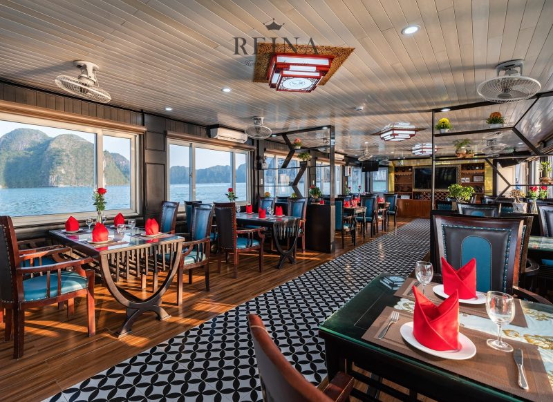 Elegant dining area on the Reina Halong Bay day cruise with set tables, panoramic windows, and scenic views of limestone islands