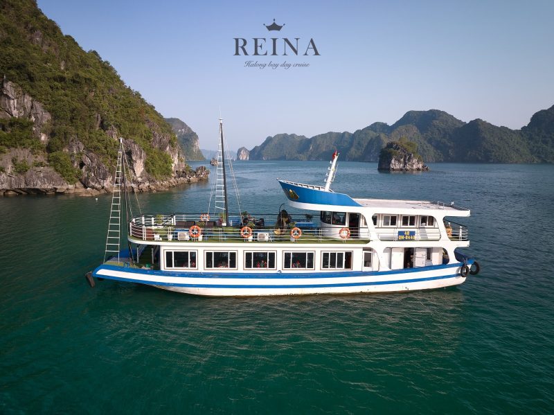 The Reina day cruise boat sailing in the serene waters of Halong Bay, surrounded by lush, rocky islands