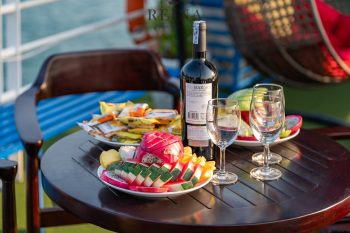 Close-up of a table with a bottle of wine, glasses, and a platter of fresh fruit on the Reina Halong Bay day cruise