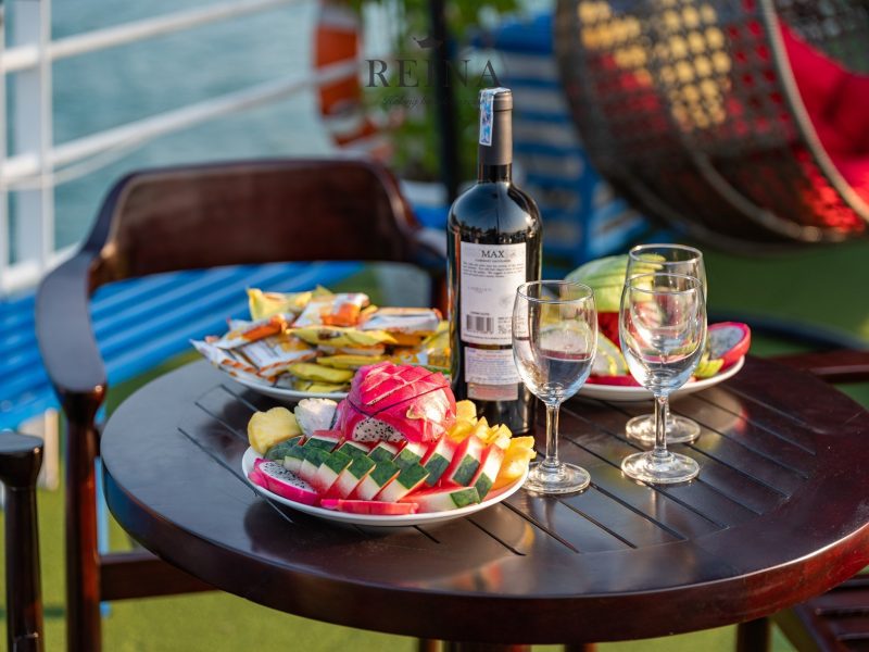 Close-up of a table with a bottle of wine, glasses, and a platter of fresh fruit on the Reina Halong Bay day cruise