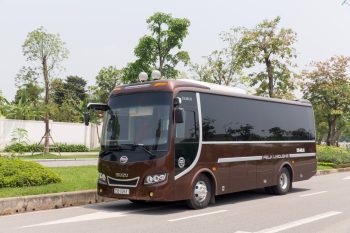 Felix Limousine 16-seater luxury bus for Hanoi to Ha Long Bay transfer, parked on a sunny day with lush greenery in the background