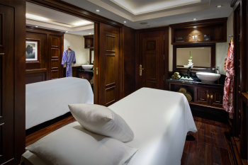 Luxurious spa treatment room on the Paradise Elegance Cruise with a massage table, elegant wood furnishings, and a serene atmosphere