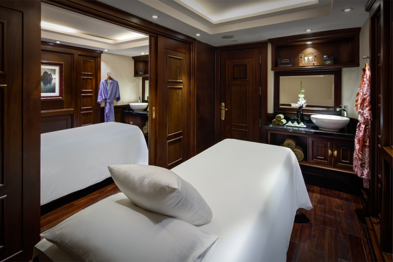 Luxurious spa treatment room on the Paradise Elegance Cruise with a massage table, elegant wood furnishings, and a serene atmosphere