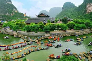 Traditional Vietnamese boats with colorful decorations on a river, surrounded by lush greenery and mountains in Ninh Binh, with a temple in the background