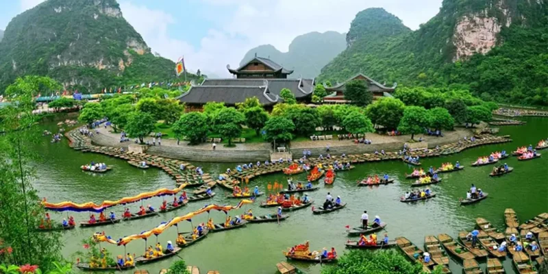 Traditional Vietnamese boats with colorful decorations on a river, surrounded by lush greenery and mountains in Ninh Binh, with a temple in the background