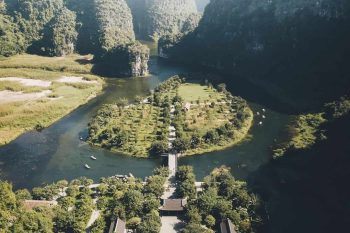 Aerial view of Ninh Binh's stunning landscape featuring lush greenery, karst mountains, and traditional temples surrounded by a river