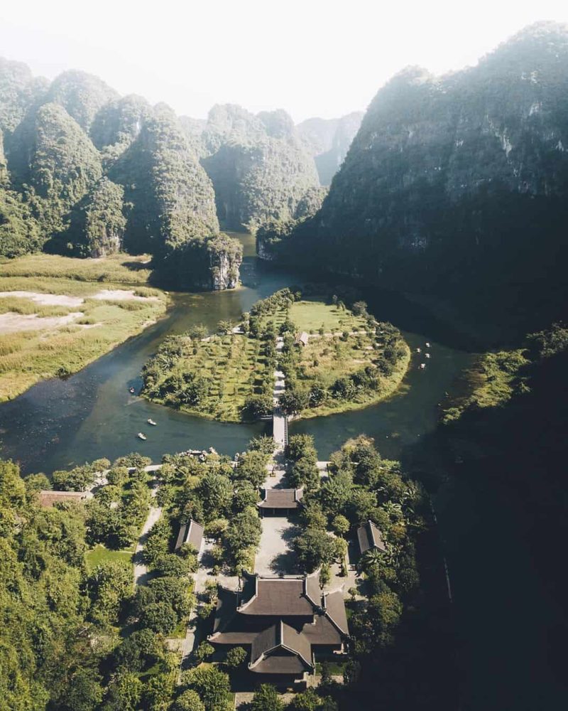 Aerial view of Ninh Binh's stunning landscape featuring lush greenery, karst mountains, and traditional temples surrounded by a river