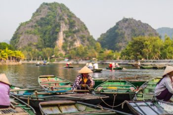 Traditional rowing boats on a river in Ninh Binh with limestone mountains in the background and people wearing conical hats