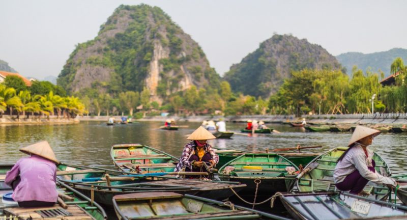 Traditional rowing boats on a river in Ninh Binh with limestone mountains in the background and people wearing conical hats
