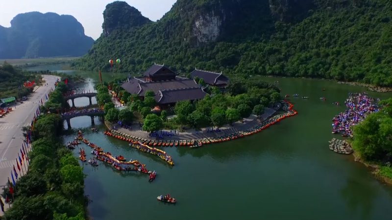 Aerial view of Trang An in Ninh Binh with traditional boats on the river, lush green mountains, and ancient temples