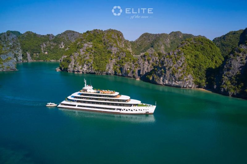 A luxurious cruise ship, Elite of the Seas, sailing through the emerald waters of Halong Bay, surrounded by limestone karsts and lush greenery