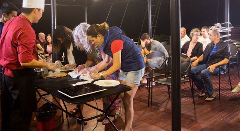 Guests participating in a cooking class on the deck of the Orchid Trendy Cruise, Ha Long Bay, Vietnam - Learning to make traditional Vietnamese dishes