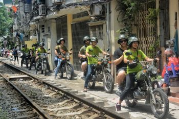 Tour guide and tourists on motorbikes exploring Hanoi's night markets and vibrant streets.