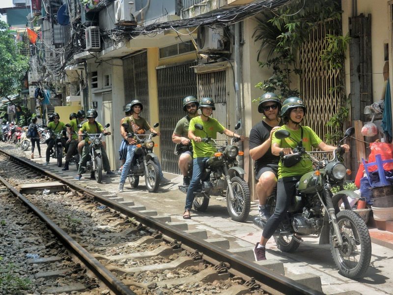 Tour guide and tourists on motorbikes exploring Hanoi's night markets and vibrant streets.