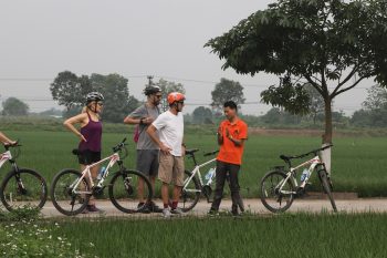 Group of tourists biking through Hanoi's narrow alleys, experiencing the city's local life and culture.