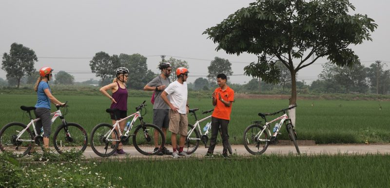 Group of tourists biking through Hanoi's narrow alleys, experiencing the city's local life and culture.