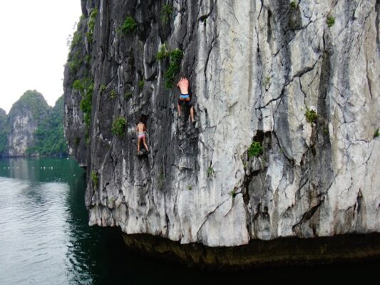 Tourists rock climbing on limestone cliffs in Ha Long Bay