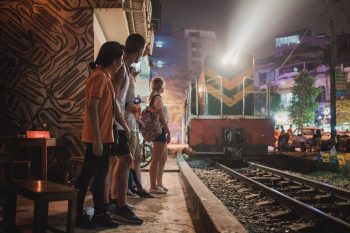 Tourists watching a train pass by in Hanoi, experiencing the unique local culture and nightlife.