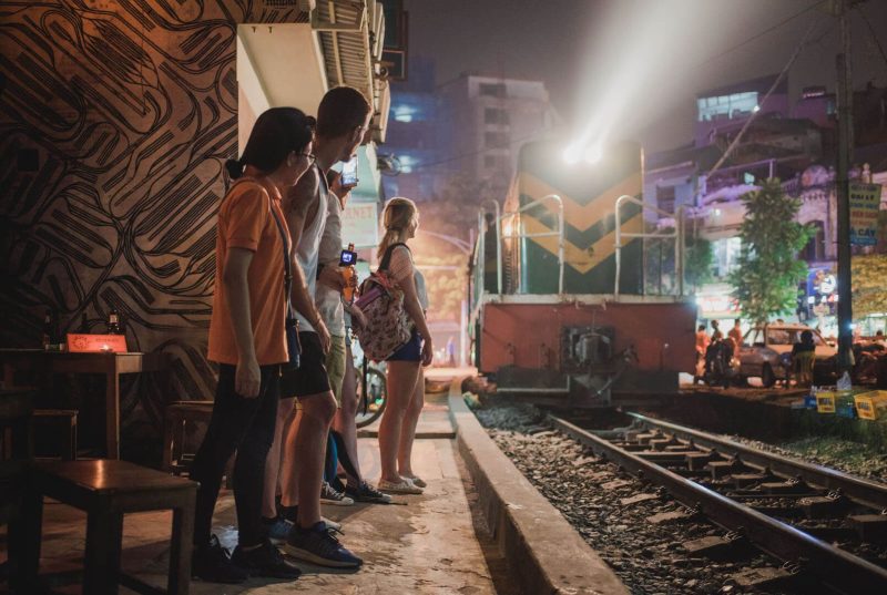Tourists watching a train pass by in Hanoi, experiencing the unique local culture and nightlife.