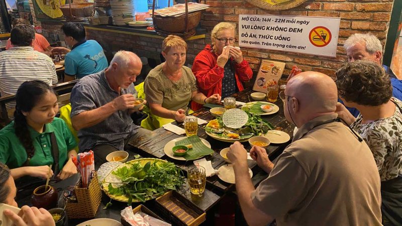 Tourists enjoying banh xeo rolls in Hanoi, experiencing the local cuisine and nightlife.