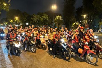 Tour guide and tourist on a motorbike exploring Hanoi's vibrant streets at night.