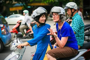 Tour guide riding a motorbike with a tourist in Hanoi at night, exploring the city's vibrant nightlife.