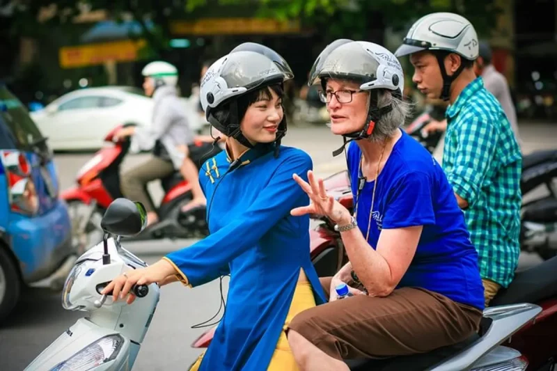 Tour guide riding a motorbike with a tourist in Hanoi at night, exploring the city's vibrant nightlife.