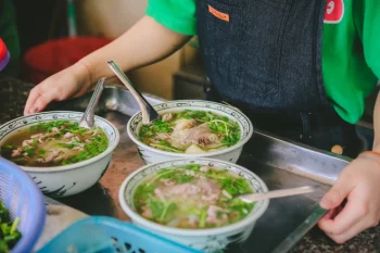 Pho Bo (Vietnamese Beef Noodle Soup) being served - A popular dish enjoyed by travelers on LuxcoTravels' Hanoi tours, including Ha Long Bay cruise trips