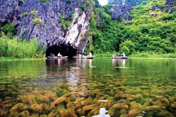 Tourists in a boat exploring a cave with clear waters at Van Long Natural Reserve, showcasing the serene beauty of Vietnam.