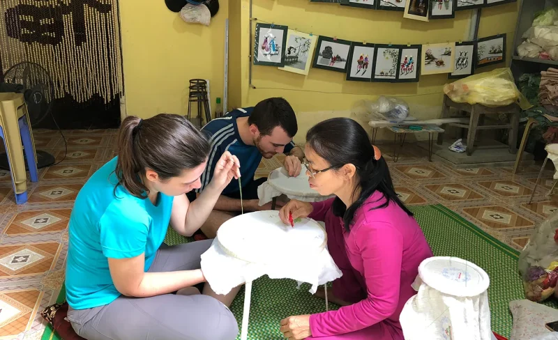 Tourists learning embroidery at Van Long Natural Reserve, experiencing traditional Vietnamese crafts.