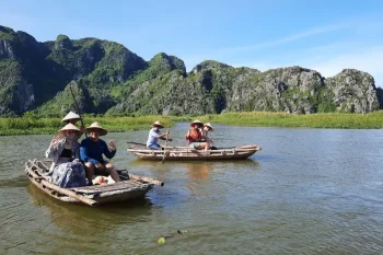 Tourists sitting in a small boat at Van Long Natural Reserve, enjoying the scenic beauty and peaceful environment.