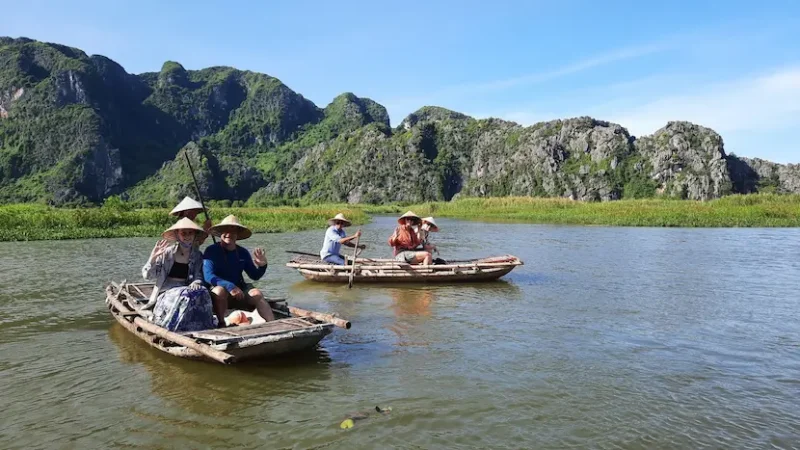 Tourists sitting in a small boat at Van Long Natural Reserve, enjoying the scenic beauty and peaceful environment.