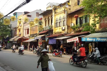 Hanoi Old Quarter with traditional buildings and people riding motorbikes, experiencing Vietnamese cultural heritage.