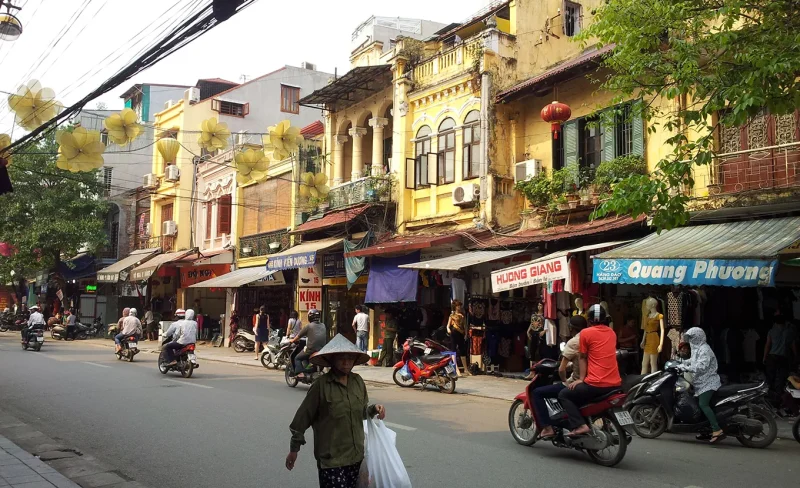 Hanoi Old Quarter with traditional buildings and people riding motorbikes, experiencing Vietnamese cultural heritage.